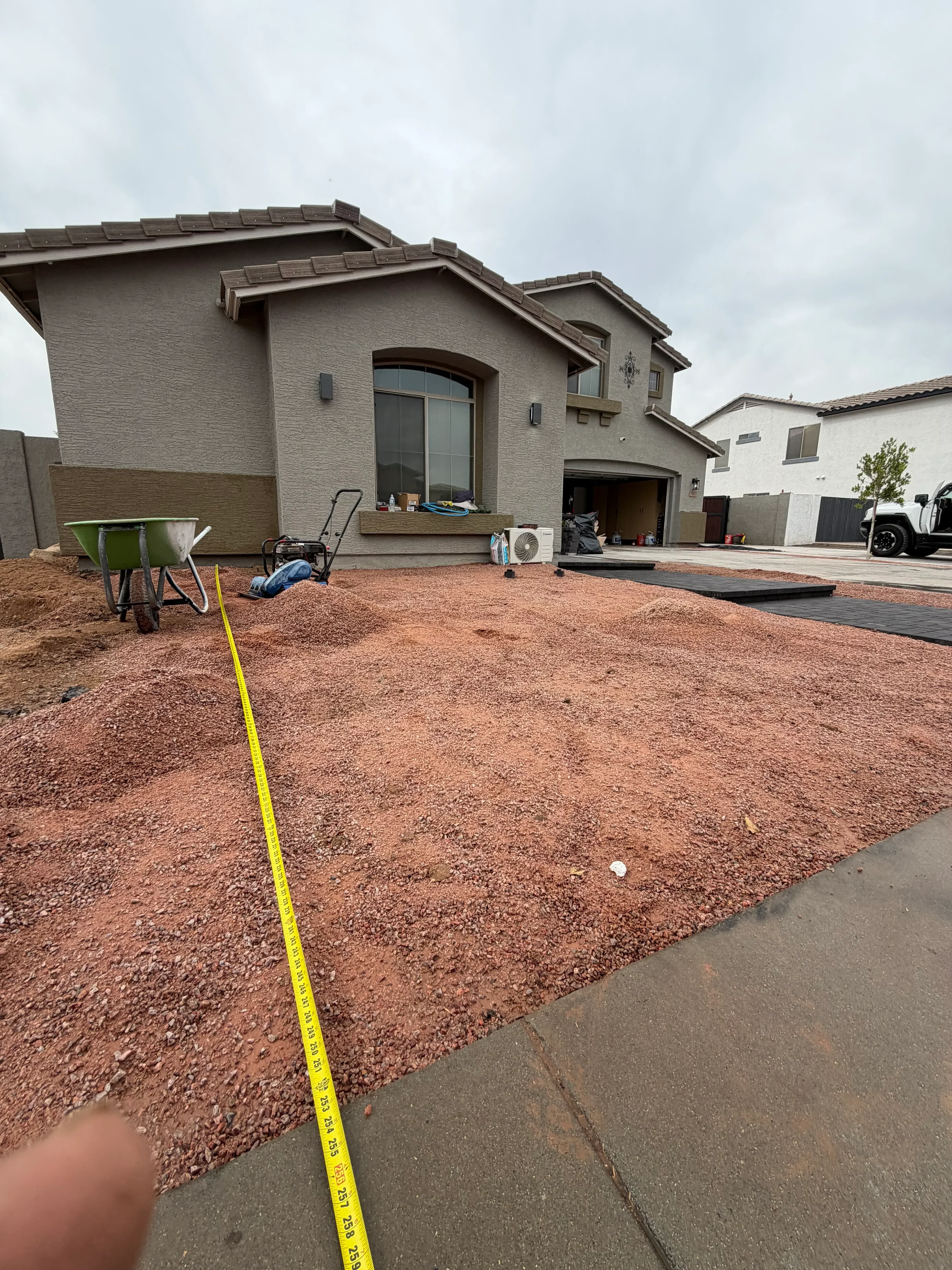 Residential driveway grading with compacted red stone base material and measuring tape