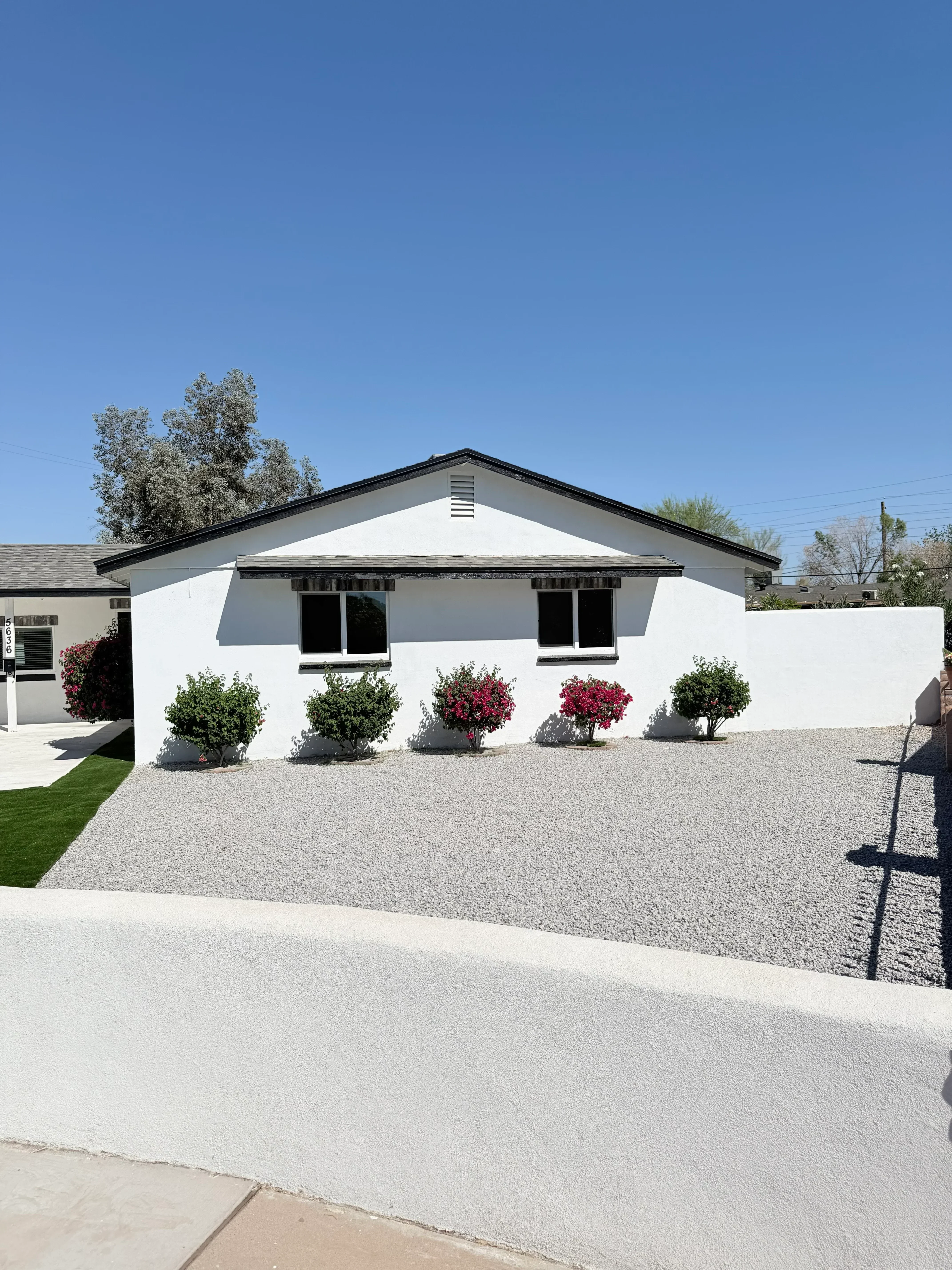 White stucco house with red flowering and green foliage container plants, gravel hardscape, and lawn
