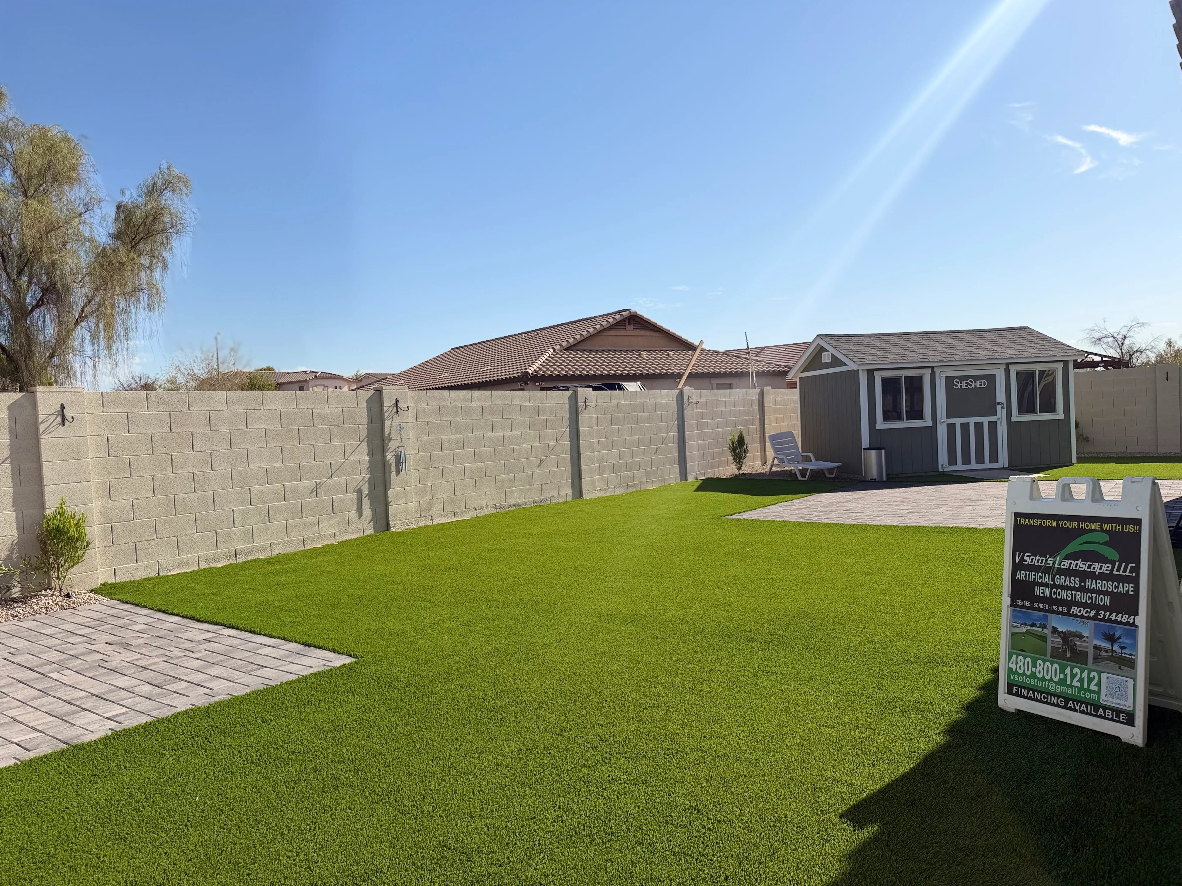 Artificial turf lawn with concrete block fence, paver patio, and storage shed in residential backyard