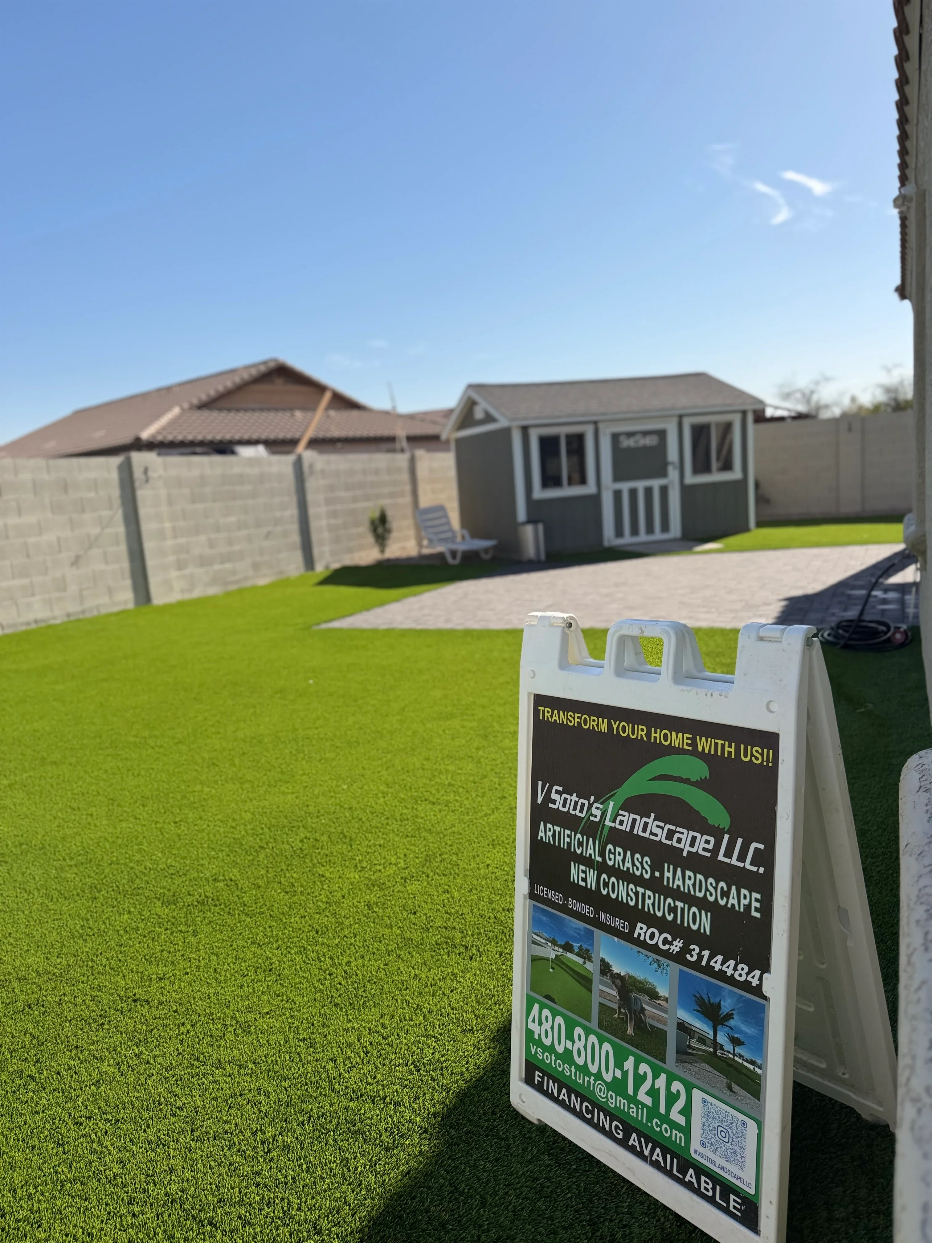 Bright green artificial grass yard with concrete driveway, storage shed, and garage