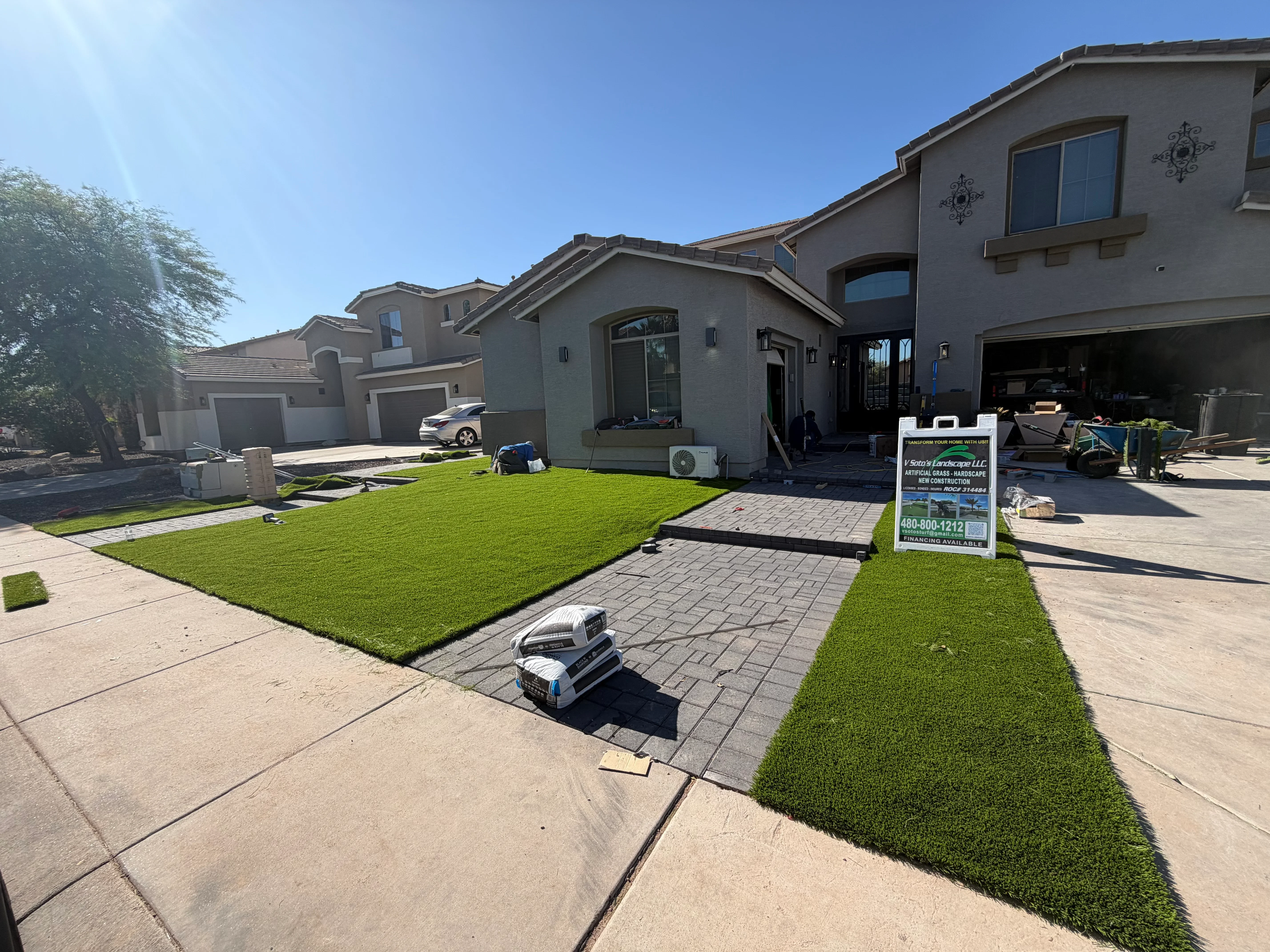 Newly installed synthetic turf lawn with gray paver walkway and driveway in front of residential home